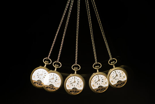 Antique pocket watch moving on a pendulum creating the illusion of multiple clocks, black background, selective focus.