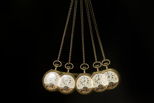 Antique pocket watch moving on a pendulum creating the illusion of multiple clocks, black background, selective focus.