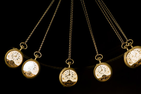 Antique pocket watch moving on a pendulum creating the illusion of multiple clocks, black background, selective focus.