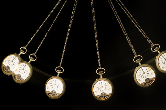 Antique pocket watch moving on a pendulum creating the illusion of multiple clocks, black background, selective focus.