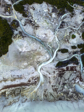 Aerial view of milky turquoise waters carving through a surreal landscape of grey and brown earth, edged with dark green vegetation, Rotorua, Waikato, New Zealand.