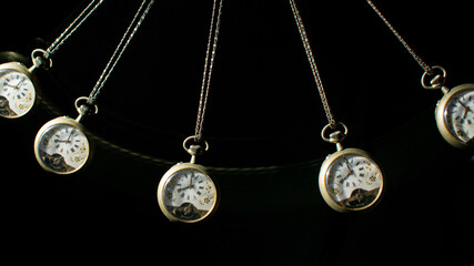 Antique pocket watch moving on a pendulum creating the illusion of multiple clocks, black background, selective focus.