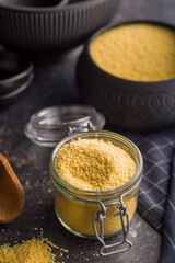 Raw couscous in jar on black table.