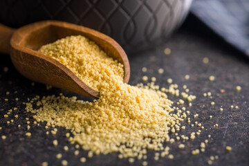 Raw couscous in scoop on black table.