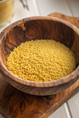 Raw couscous in bowl on wooden cutting board.