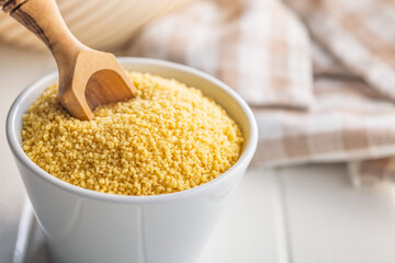 Raw couscous in bowl on white table.