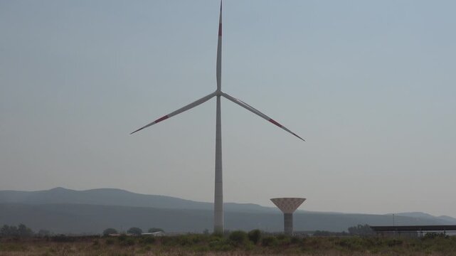 Oristano, Sardinia, Italy A large wind turbine and water tower over an agricultural landscape. 