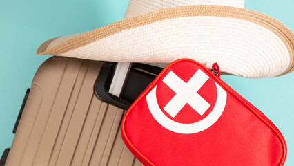 Close-up of travel suitcase, hat and first aid kit on pastel blue background. Preparing for travel,...