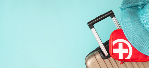 Beige travel suitcase, hat and red first aid kit on pale blue background. Travel safety, take a...