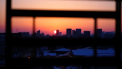 Obraz premium City skyline silhouetted against a fiery sunset through a window