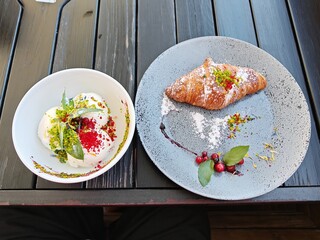 On the wooden table there is a ceramic plate with a croissant and cranberries and a ceramic bowl...