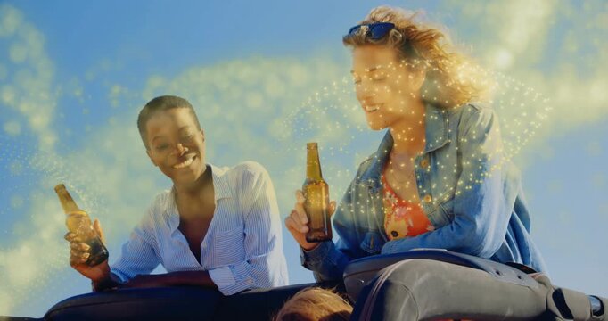 Two women perching on tailgate holding beer starting golden effect swirling around for beverage ad