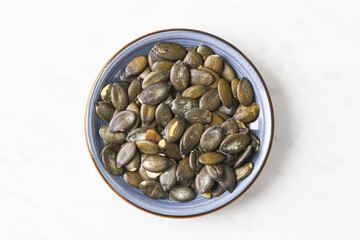 Bowl of roasted pumpkin seeds on white background. Healthy snack with natural texture. Top view of ceramic dish filled with crunchy seeds. Vegan protein food. Organic plant-based ingredient concept.