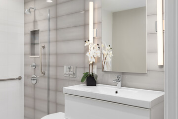 A bathroom detail with a white cabinet, grey glass rectangle tiled accent wall, and a shower with a chrome faucet and niche.