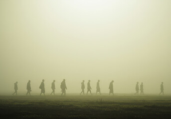 Silhouettes of people walking in a dense ethereal fog with a soft golden light illuminating the scene