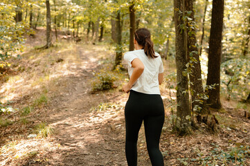 A young woman joyfully runs along a beautifully serene forest path, fully immersed in the beauty of...