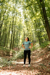 Obraz premium A woman stands confidently in the vibrant green forest, fully enjoying the tranquility of nature around her