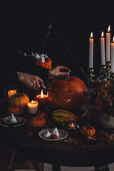 Elegant holiday party table. Female carving large orange pumpkin for Halloween party on wooden...