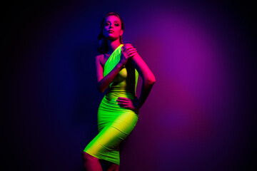 Trendy young woman in neon green dress posing under vibrant ultraviolet lighting with colorful...