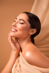 Attractive brunette woman smiling with radiant skin and elegant style, beige background...