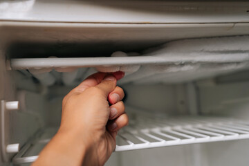Close-up of male hand removing frost accumulation from refrigerator freezer compartment,...