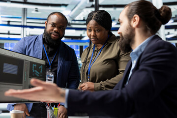 Multiethnic group of factory engineers in business attire checking equipment and manufacturing...