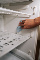 Vertical cropped shot of unrecognizable person defrosting and cleaning interior of refrigerator...