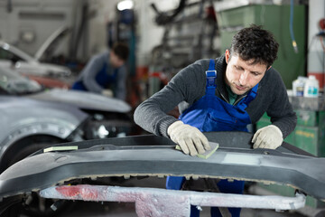 Man auto mechanic performs car body work in auto repair shop. Male auto mechanic handle polishes...