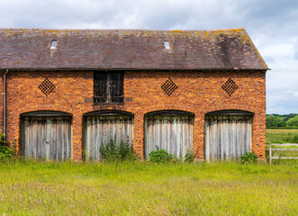A weathered brick barn with four wooden doors sits in a field in the English countryside of Shropshire