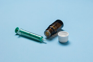 A close-up image of a medical syringe, a brown glass vial with its cap removed, and a plastic...