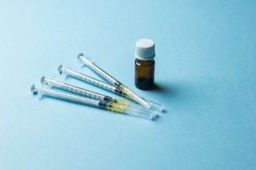 A close-up image of a medical syringe, a brown glass vial with its cap removed, and a plastic...