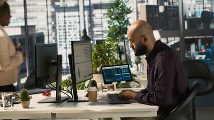 Arab office clerk working to hit key performance targets for revenue, profitability and operational efficiency. Middle Eastern employee at PC desk doing research analysis, camera A