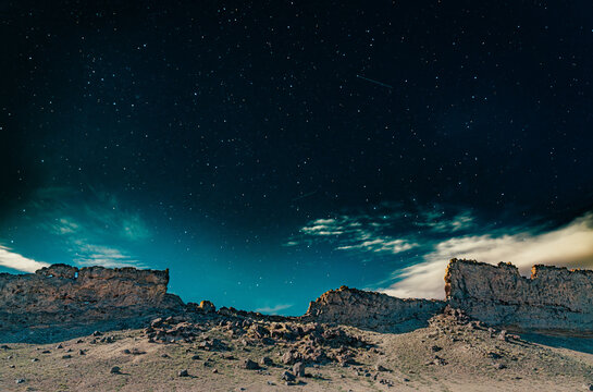 Dramatic night sky filled with countless stars and meteor trails above rugged desert cliffs. 
