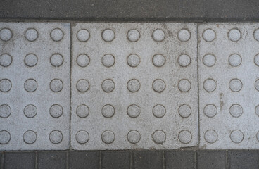 Tactile paving tiles with raised dots on a sidewalk, designed to assist visually impaired...