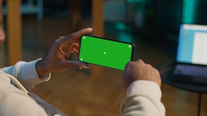 African american person using device with green screen from the comfort of his modern trendy home,...