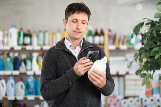 Attentive middle-aged man scanning barcode on liquid hand soap at household goods shop