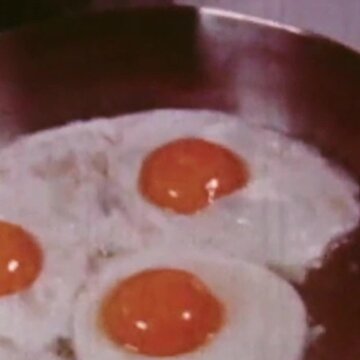 Three sunny-side-up eggs frying in a metal pan. Vintage. Retro. 