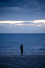 A person standing on the shore of Lake Michigan on a cloudy evening just after sunset