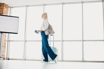 Female traveler at the airport terminal waiting with luggage and passport, showcasing a casual style and tourism concept