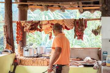 Traditional Colombian outdoor kitchen with hanging meats and man grilling