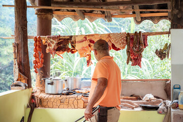 Colombian rustic kitchen with hanging meats and man grilling outdoors