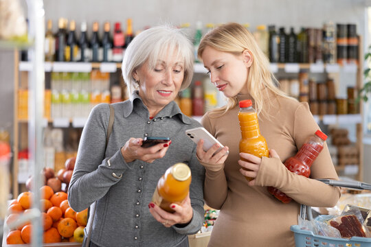 Elderly mother and her adult daughter scan a QR code on a tomato and peach juice label together to check the expiration date