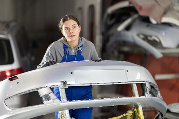 Service station girl worker performs car repairs, assembles and connects parts of car body. Worker...
