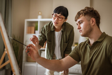 Art teacher guiding student painting on canvas in art class