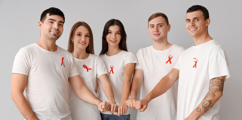 Group of young people with red ribbons putting hands together on grey background. World AIDS day concept