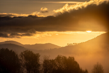 Golden hour bathes mountainous landscape in a misty glow as the sun breaks through the clouds.