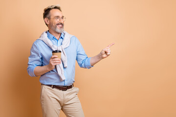 Confident mature businessman holding coffee and gesturing with a point on a beige background,...