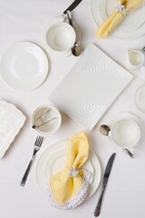 Tea setting for two with white dishes and yellow napkins on a light tablecloth, top view.