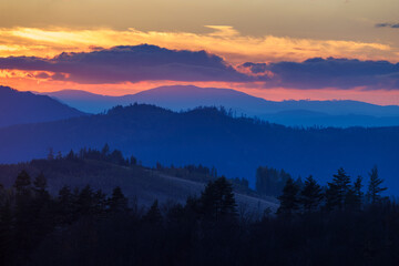 Layered mountain ranges illuminated by vibrant sunrise, casting long shadows in the twilight...
