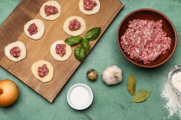 Wooden board of raw dough with minced meat and ingredients for preparing dumplings on grunge background